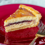 Slice of Gateau Basque with creamy custard and cherry jam filling on a red plate