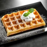 Gaufre de Bruxelles dorée et croustillante, saupoudrée de sucre glace et garnie de crème fouettée et de feuilles de menthe.
