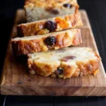 Pudding au pain maison aux raisins secs, moelleux à l’intérieur et doré à l’extérieur, découpé en tranches sur une planche en bois.