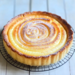 A freshly baked tarte au fromage blanc with a golden spiral top, lightly dusted with powdered sugar, cooling on a wire rack.