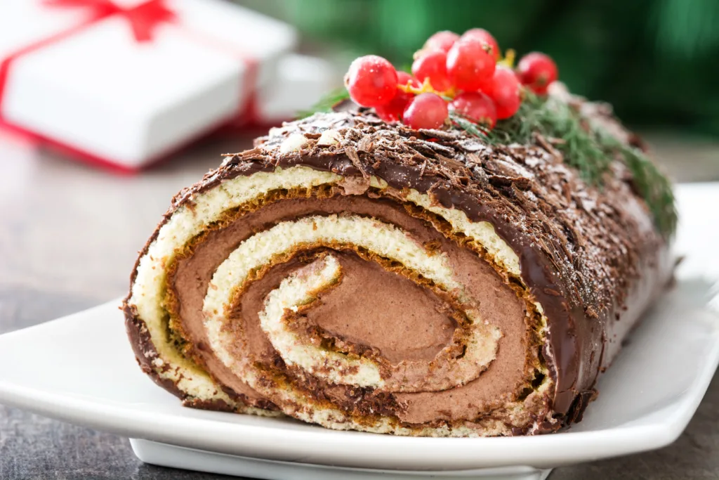 Bûche de Noël made with rolled sponge cake, creamy filling, nut coating, and festive chocolate decorations