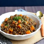 Bol de recette lentilles vertes cuites avec carottes et herbes fraîches servi dans un plat blanc rustique