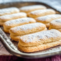 French biscuit cuillère dusted with powdered sugar and served on a white plate.