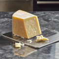 A wedge of authentic Grana Padano AOP cheese on a grater with freshly shaved cheese flakes.