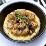 Ris de veau dorés servis sur une purée crémeuse avec champignons, échalotes et sauce à la crème dans un bol noir.