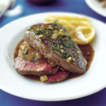 Juicy bavette de bœuf cooked medium rare and topped with a rich shallot sauce, served on a white plate with fresh parsley and lemon slices.